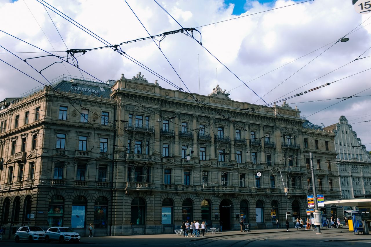 A historic Credit Suisse building in Zurich with tram wires overhead.