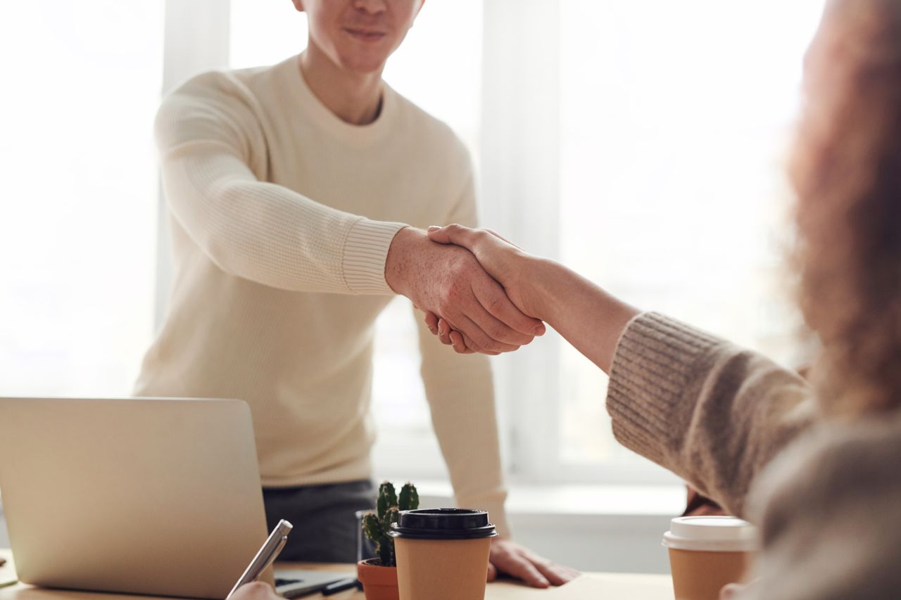 Two people shaking hands over a desk in an office.