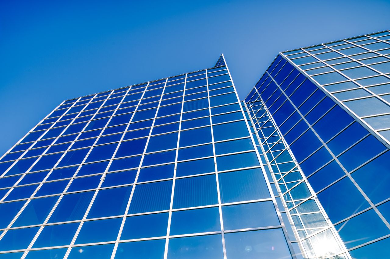 From below of multistory modern tall building with geometric design and large windows under clear bright blue sky